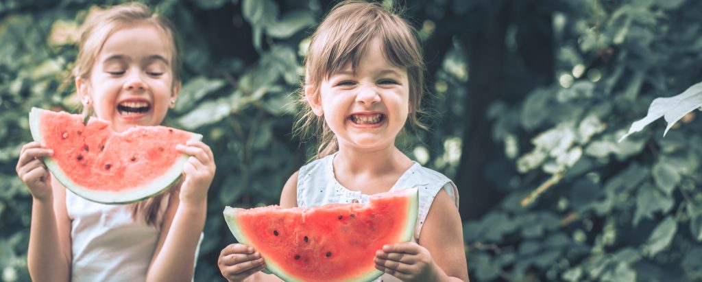 two little cute girls eating watermelon outdoors